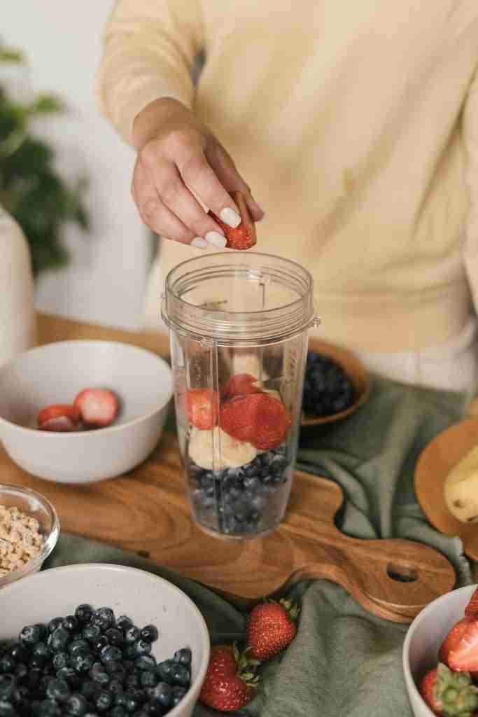 Person adding strawberries and bananas to a smoothie as a post-workout meal rich in carbs and protein for recovery.