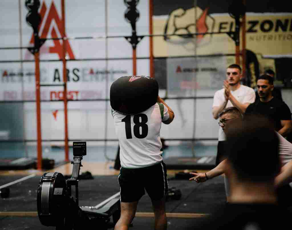 Athlete performing a sandbag carry over the shoulder during a competition, demonstrating functional strength training under load
