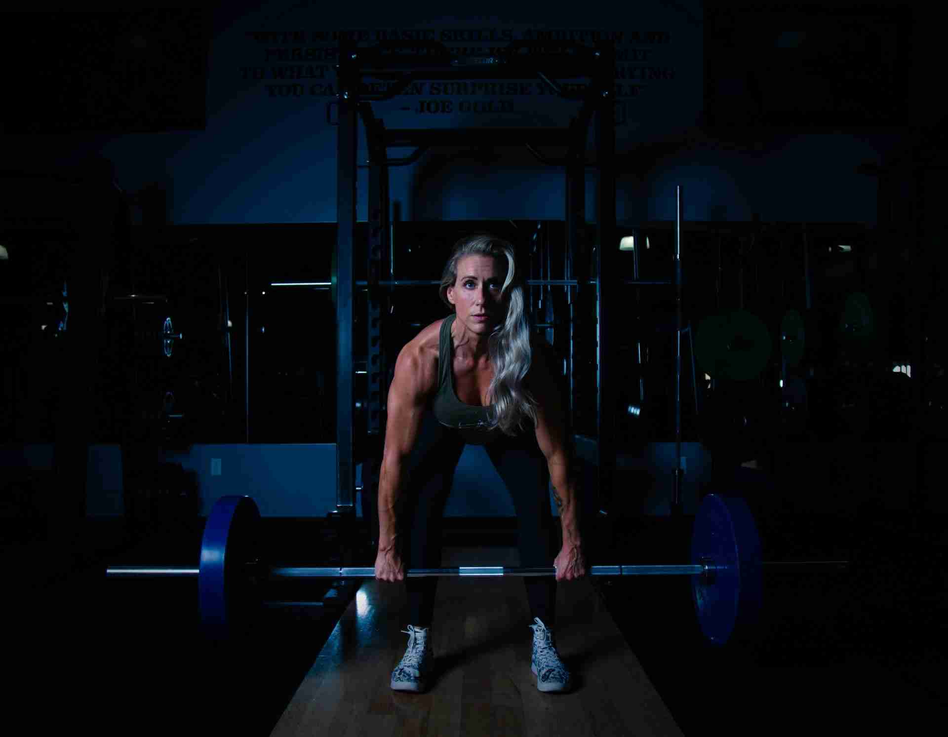 Woman lifting barbell in gym demonstrating strength training for muscle building