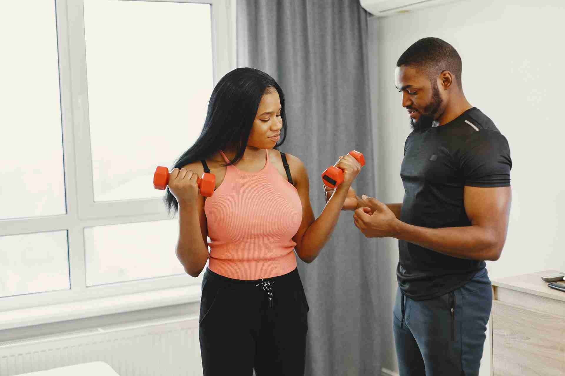In-home personal trainer coaching client with dumbbells during home training session