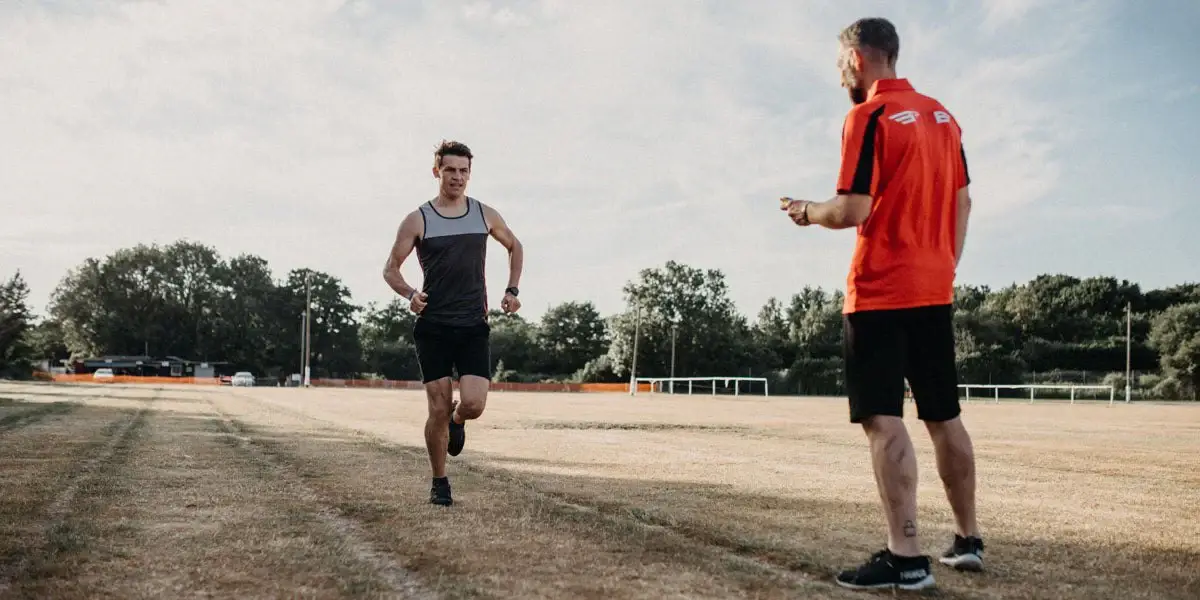 Running coach observing athlete's form and gait during track training session in Toronto