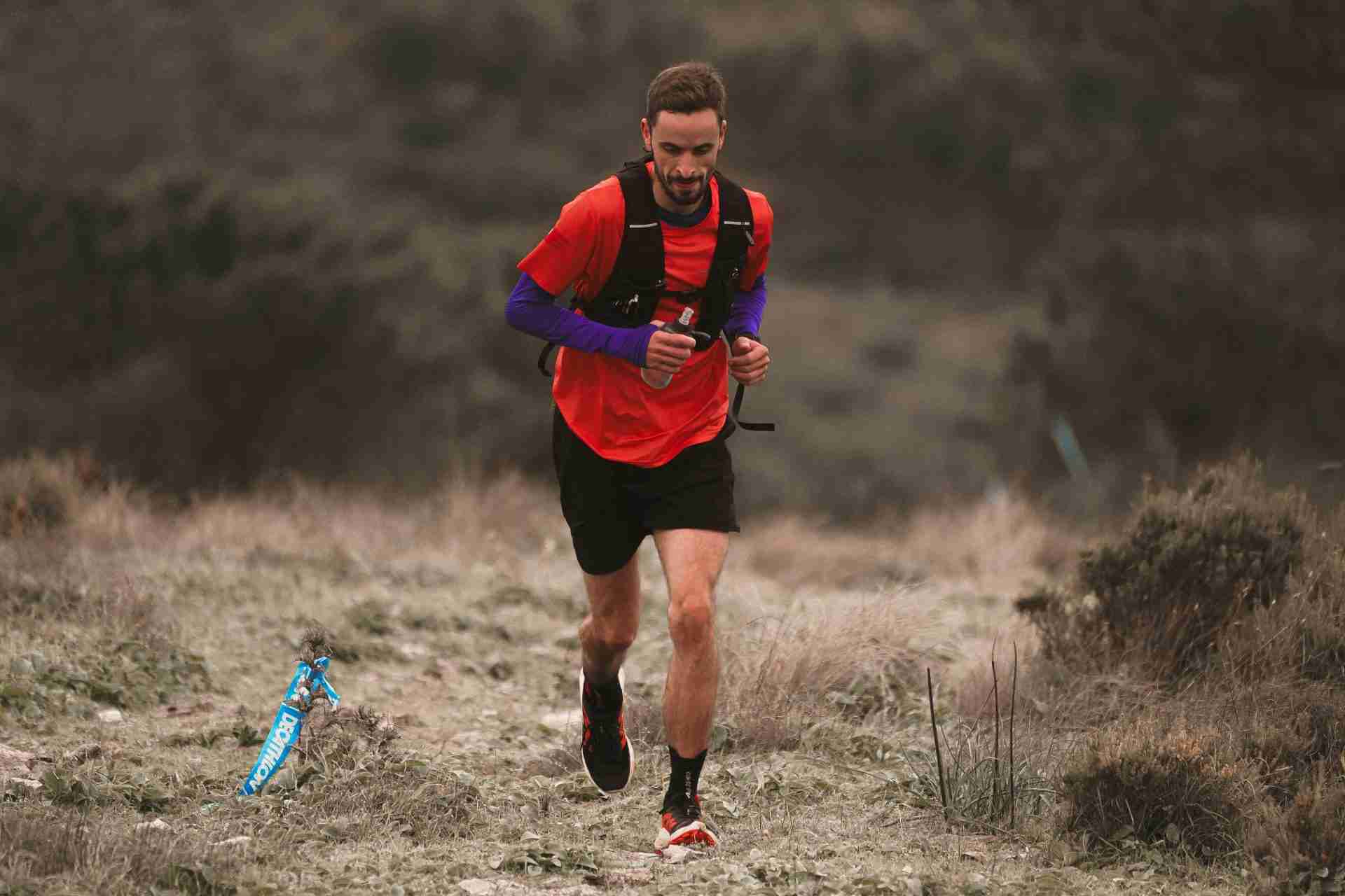 Runner wearing hydration vest and compression socks on trail showing essential running gear